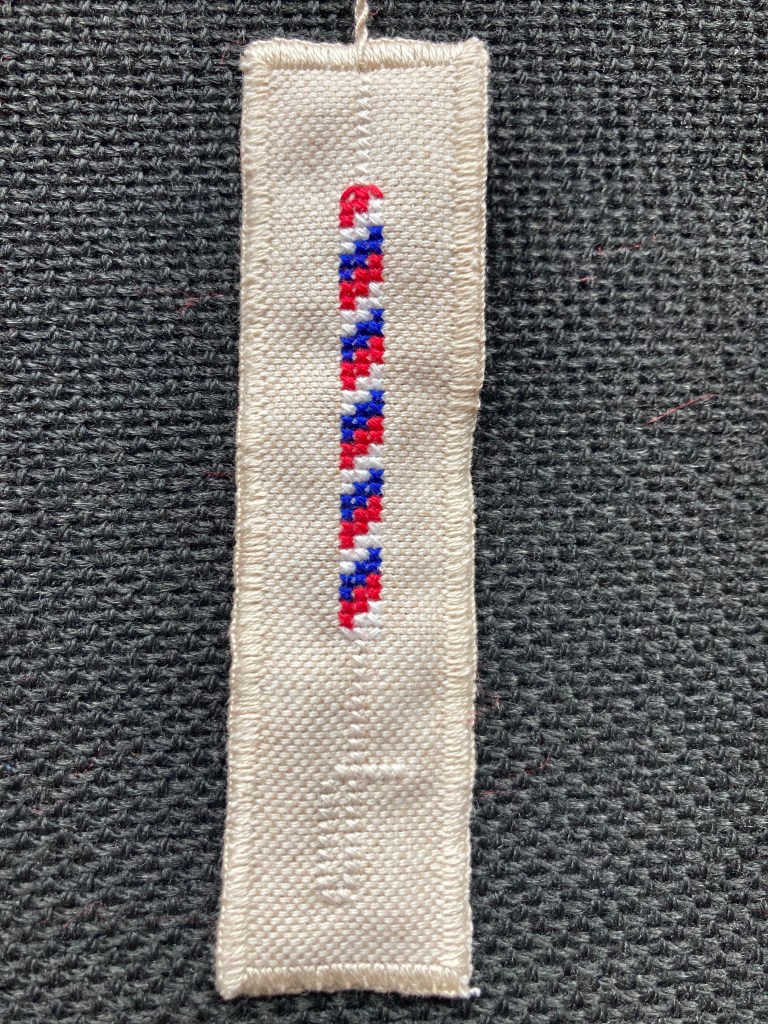 A cloth bookmark with a cross-stitch bell rope on it